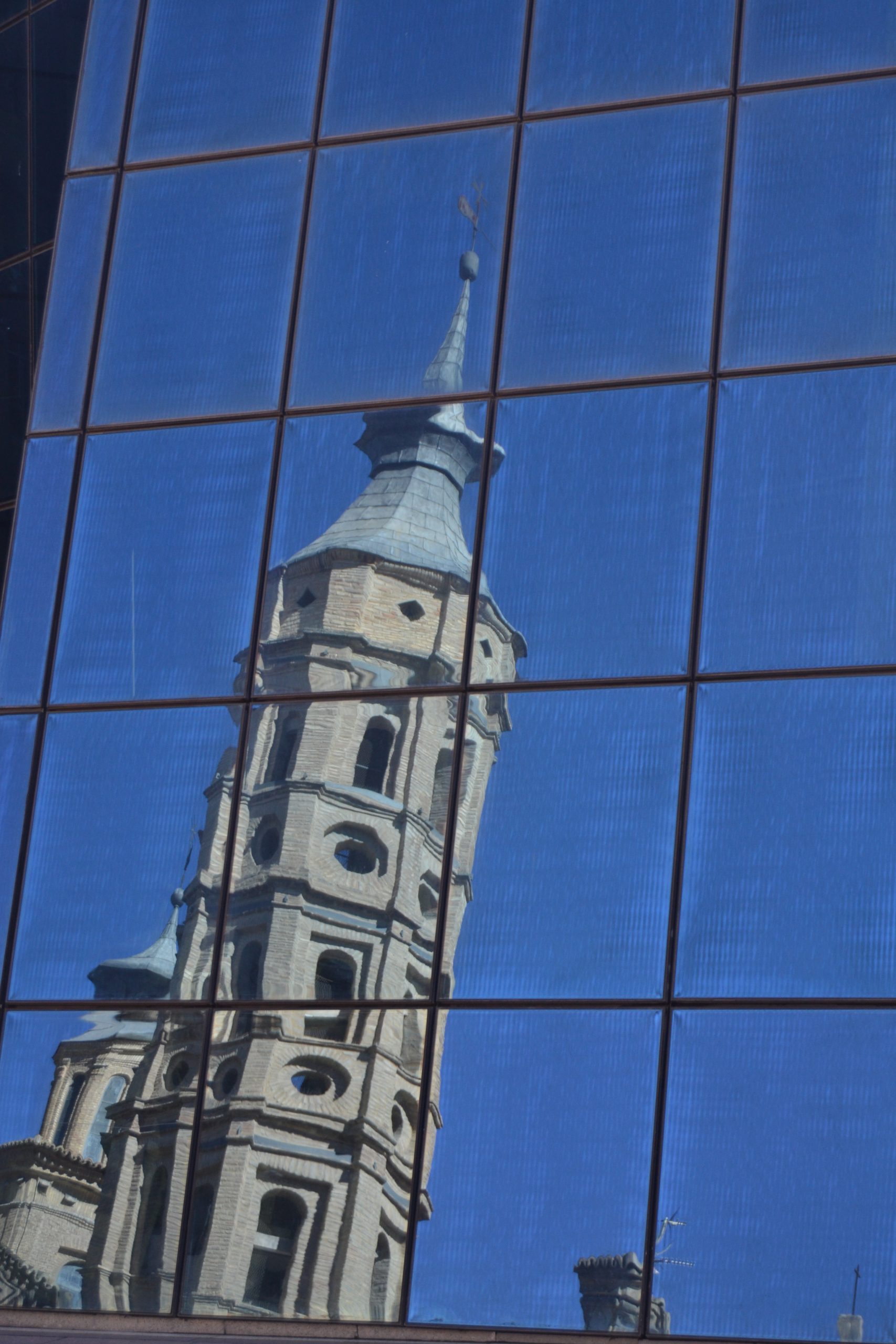 Torre de la Iglesia de San Juan de los Panetes refeljada en los cristales del parking